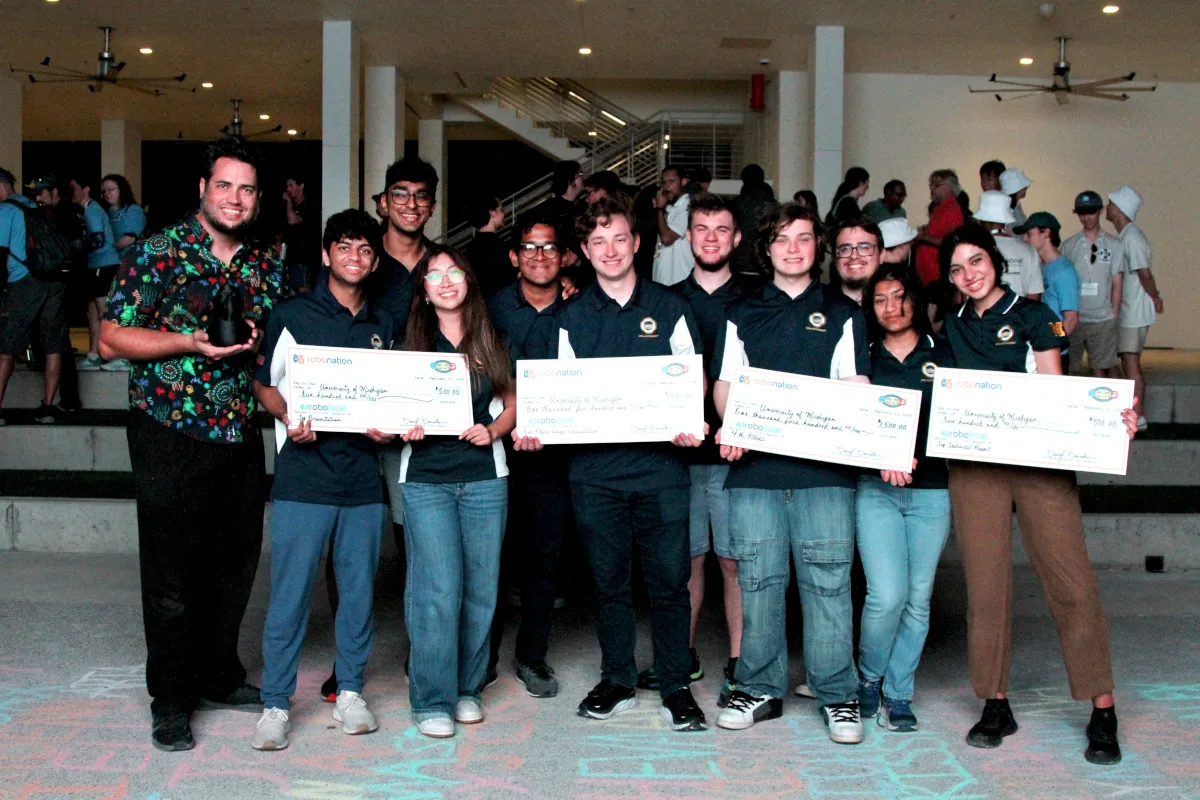 UM::Autonomy members pose on-stage with a judge holding a banner reading "2023 3rd place design documentation"