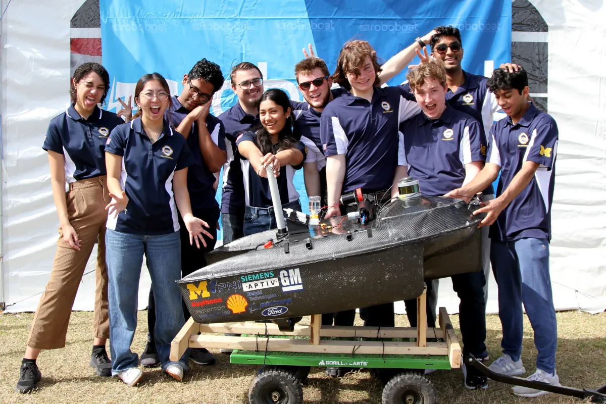 The UM::Autonomy members in a fun pose surrounding the boat